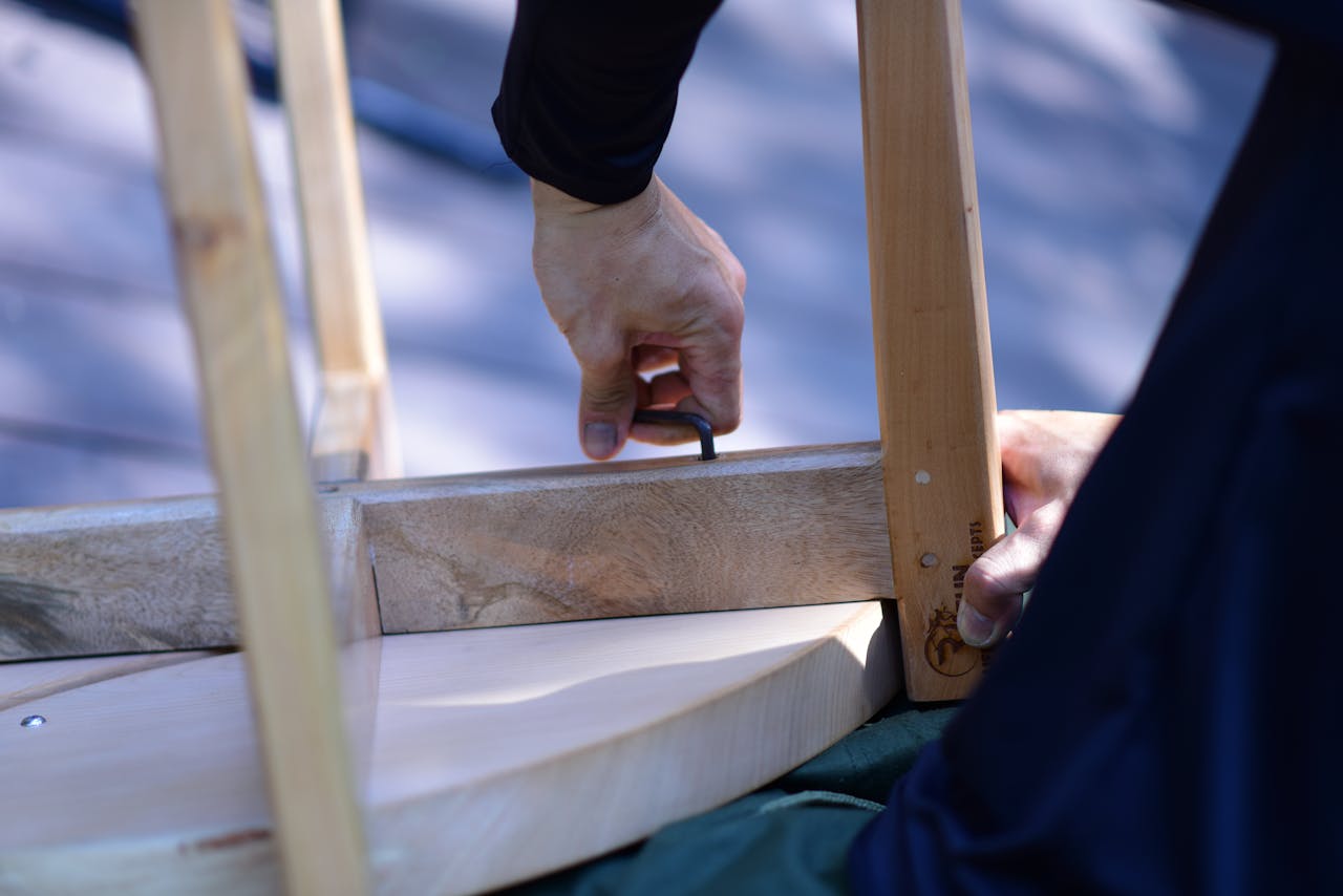 Close-up of a person assembling wooden furniture with an Allen wrench on a sunny day.