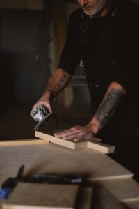 A focused craftsman polishing wood with a grinder in his workshop, showcasing professional skill and technique.